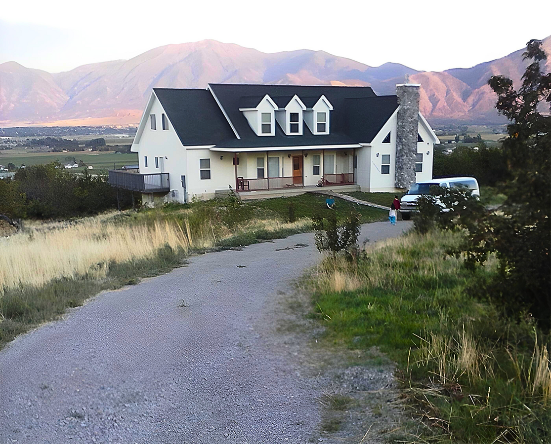White house with dark green roof, surrounded by cherry trees, with mountains in background