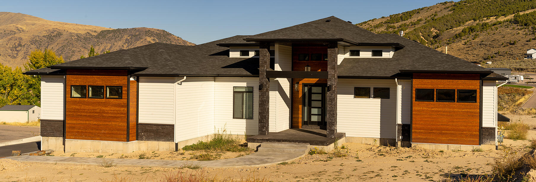 White and brown house with orange-brown accents, on slope of mountain